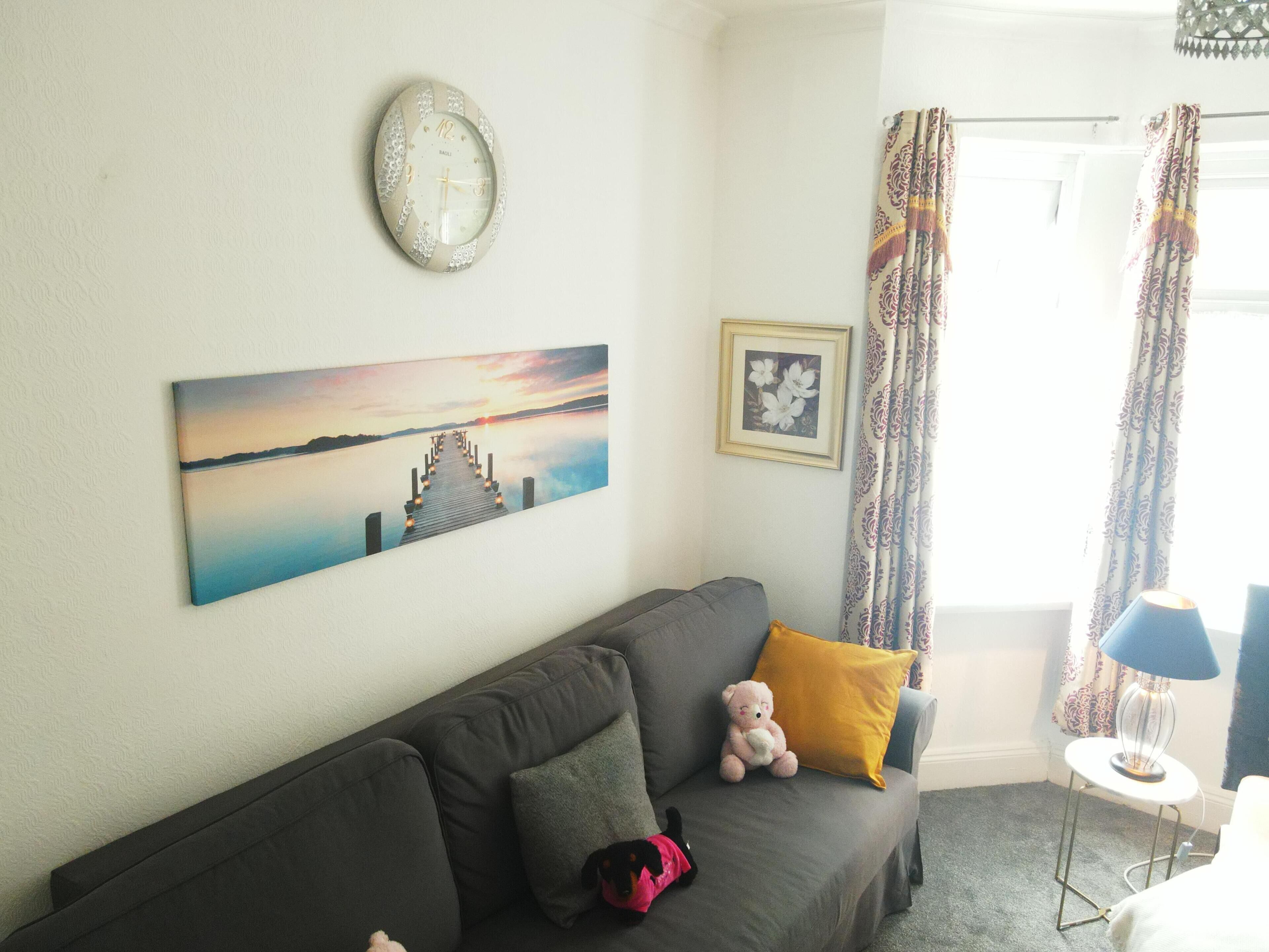Un salon avec un canapé, une horloge, un tableau et une lampe.