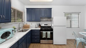A modern kitchen with dark blue cabinets, a stainless steel stove, and a white refrigerator. - Designer Poolside La Mesa Retreat w/ BBQ & Yard (La Mesa)
