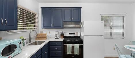 Una cocina moderna con armarios azul oscuro, estufa de acero inoxidable y refrigerador blanco.