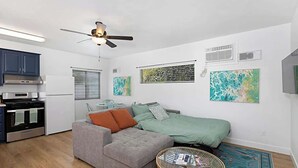 A compact living space with a kitchenette, a grey sofa, a green bed, and a wicker coffee table. - Designer Poolside La Mesa Retreat w/ BBQ & Yard (La Mesa)