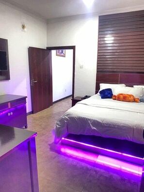 Quarto com cama, mesa de cabeceira, cabeceira de madeira e uma porta.