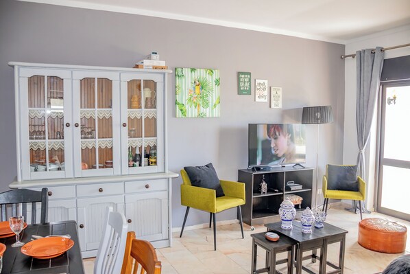 Una sala de estar con comedor, televisor y aparador con puertas de vidrio.