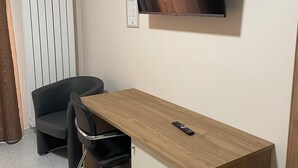 A small, modern room with a wooden desk, a black office chair, a television mounted on the wall, and a radiator.