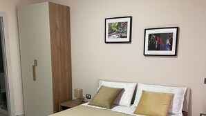 A neatly made bed with a quilted cover, a wooden wardrobe, and two framed pictures on the wall.