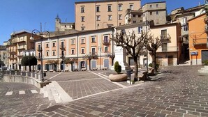 A cobblestone square with historic buildings, a fountain, and a clock tower in the background.