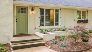 Une maison de plain-pied avec une porte verte, des fenêtres à cadre blanc et un petit jardin devant, agrémenté de différentes plantes.