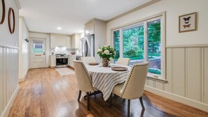 Un coin repas avec une table dressée pour quatre personnes, un réfrigérateur et une fenêtre donnant sur un paysage verdoyant.
