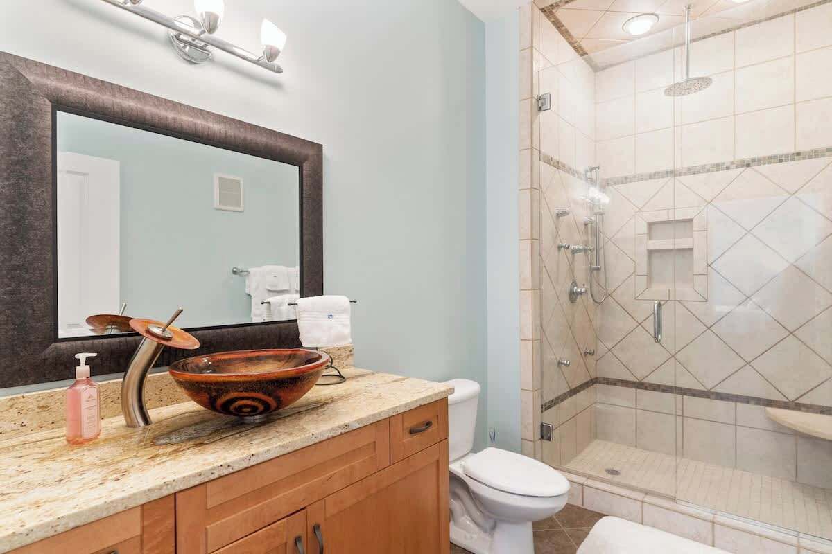 A bathroom with a large mirror, a vessel sink, a toilet, and a walk-in shower.
