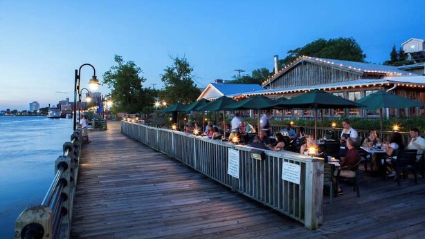 Un restaurant situé au bord de l’eau, avec une terrasse en bois offrant des places assises à l’extérieur et donnant sur un plan d’eau.