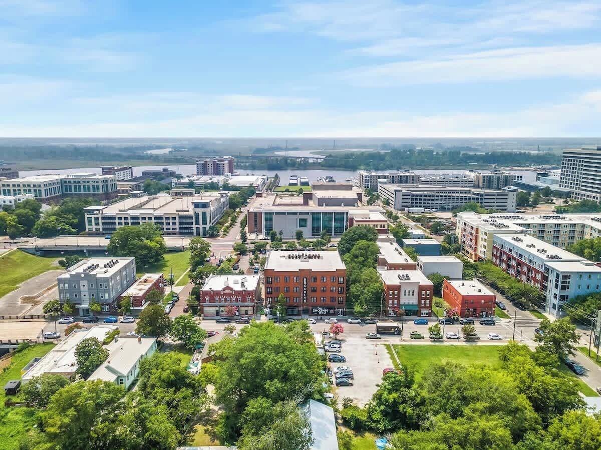Kaupunkikuva, jossa on yhdistelty moderneja ja perinteisiä rakennuksia, keskeisellä paikalla sijaitseva punatiilinen rakennus ja parkkipaikka.