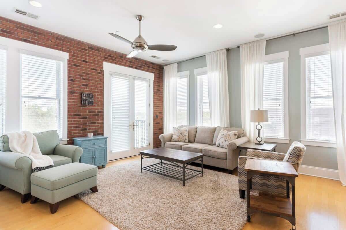 A living room with a brick wall, two sofas, a coffee table, a side table, and a ceiling fan.