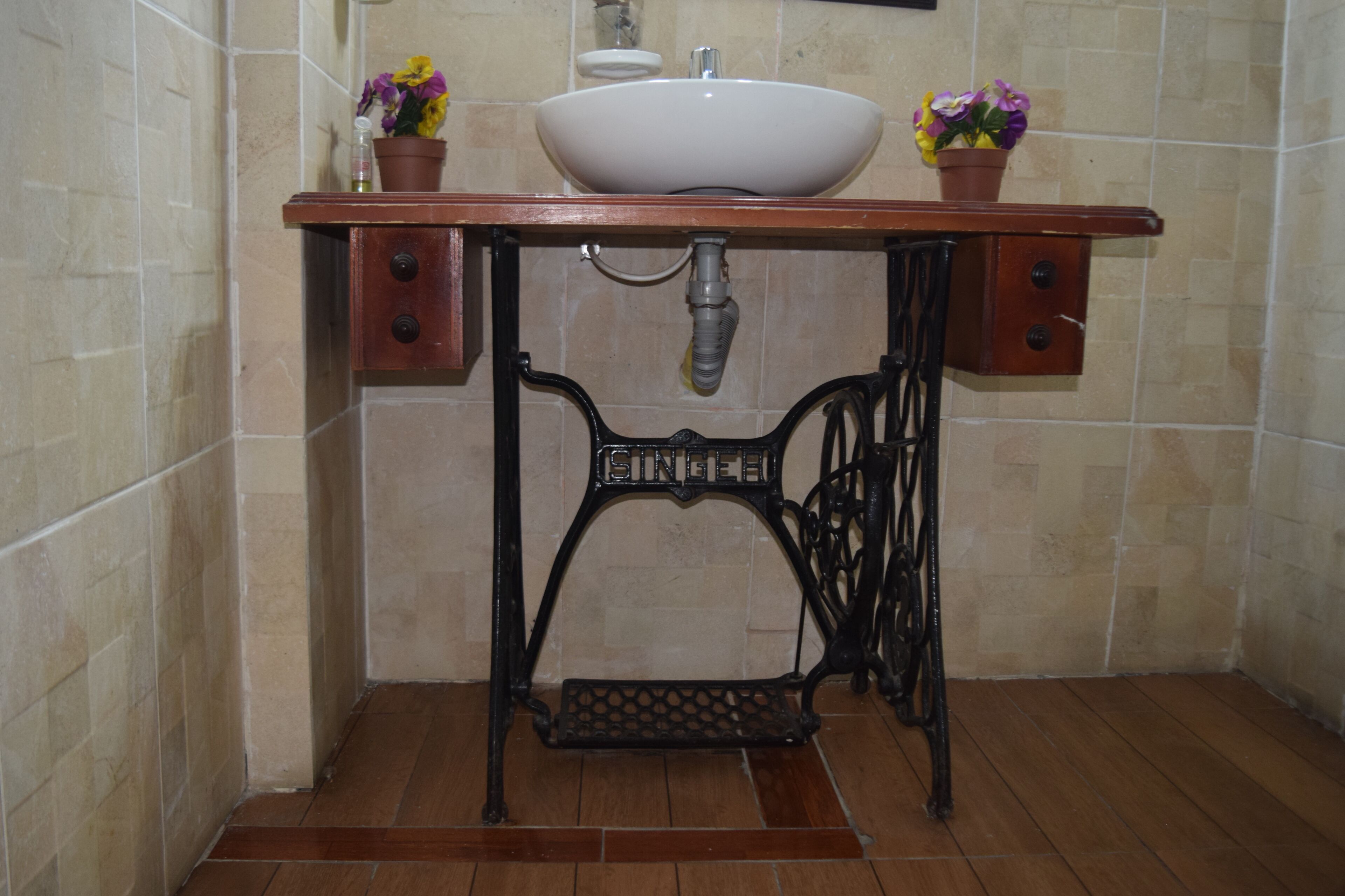 A bathroom with a sink, two potted plants, a vintage-style vanity, and tiled walls.
