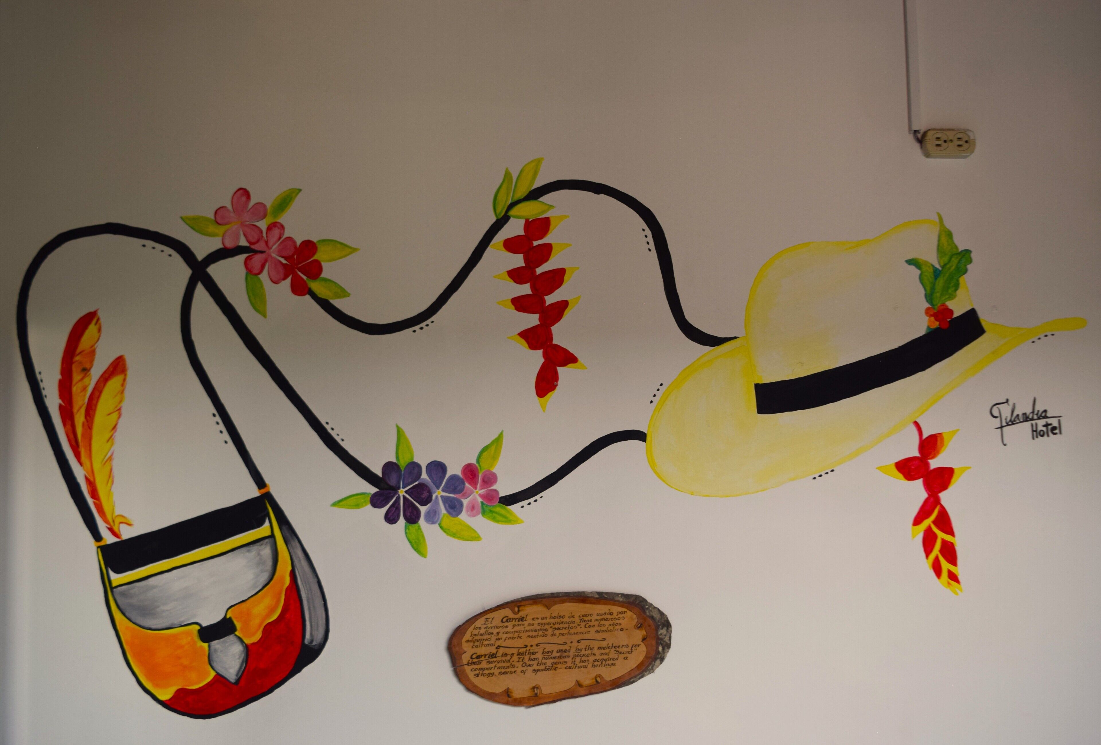 A wall with a drawing of a yellow hat, a red and yellow bag, and a plaque with text.