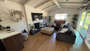 Ein geräumiges Wohnzimmer mit großem Fernseher, Holzboden, einem grauen Sofa und einem Essbereich mit Marmorarbeitsplatte.