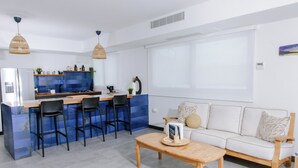 Une cuisine moderne avec un mur de crédence bleu, un îlot central doté de tabourets de bar et un canapé blanc accompagné d’une table basse.