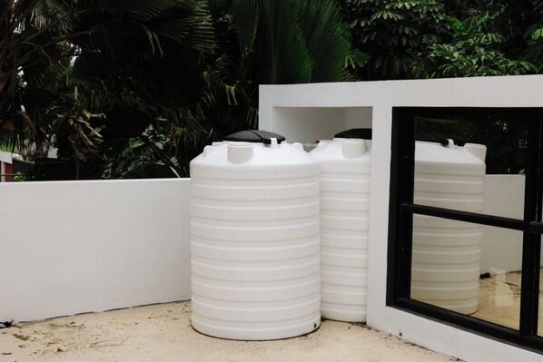 Two white storage tanks next to a white wall and a window.