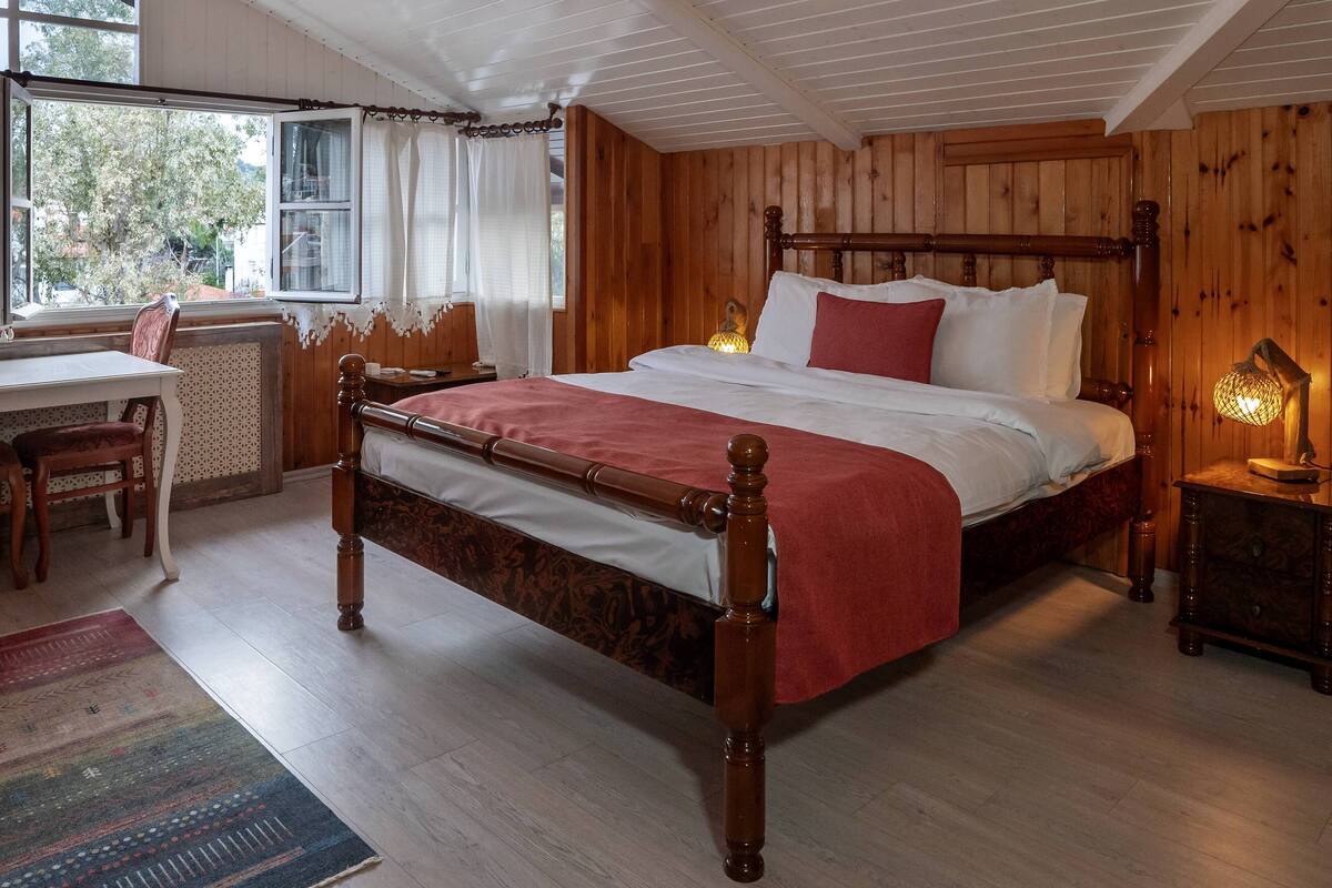 A wooden-paneled bedroom with a large bed, a desk, and a chair.