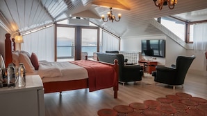 A bedroom with a bed, a desk with bottles, a TV, and a view of the sea. - Black Lotus İzmir (Izmir)