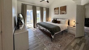 Une chambre avec un lit, un ventilateur de plafond, un bureau avec une lampe et une vue sur l’extérieur.