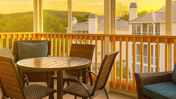 Un espace extérieur abrité, doté d’une table ronde et de chaises, d’une rambarde en bois et offrant une vue sur des maisons et des arbres.