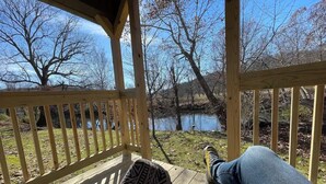 A wooden deck with a view of a pond and trees. - Meadow Riverfront Cabin
 (Nallen)
