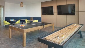 A room with ping pong tables, a foosball table, and a seating area with yellow chairs and a blue sofa. - Level Old Town - Spacious Studio Suite (Chicago)