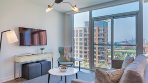 A modern living room with a sofa, a desk, a chair, a small table, and a TV. - Level Old Town - Spacious Studio Suite (Chicago)