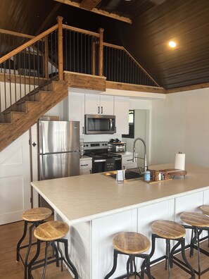 Une cuisine moderne dotée d’un îlot central, d’appareils électroménagers en acier inoxydable et de tabourets de bar en bois.