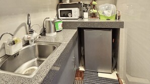 Een compacte keuken met grijze kastjes, een ingebouwde magnetron, een spoelbak en een kleine koelkast.
