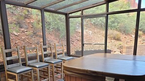 Un bain à remous doté de chaises en bois et d’une enceinte en verre donnant sur un espace extérieur rocheux.