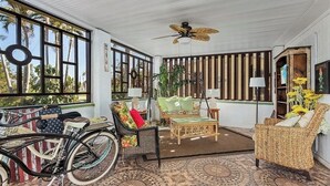 Una habitación soleada con muebles de mimbre, una bicicleta y un ventilador de techo.