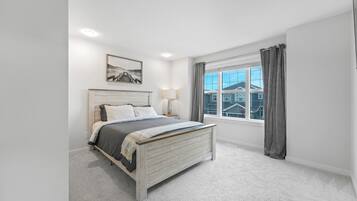 A bedroom with a bed, a window with curtains, a bedside lamp, and a framed picture on the wall.