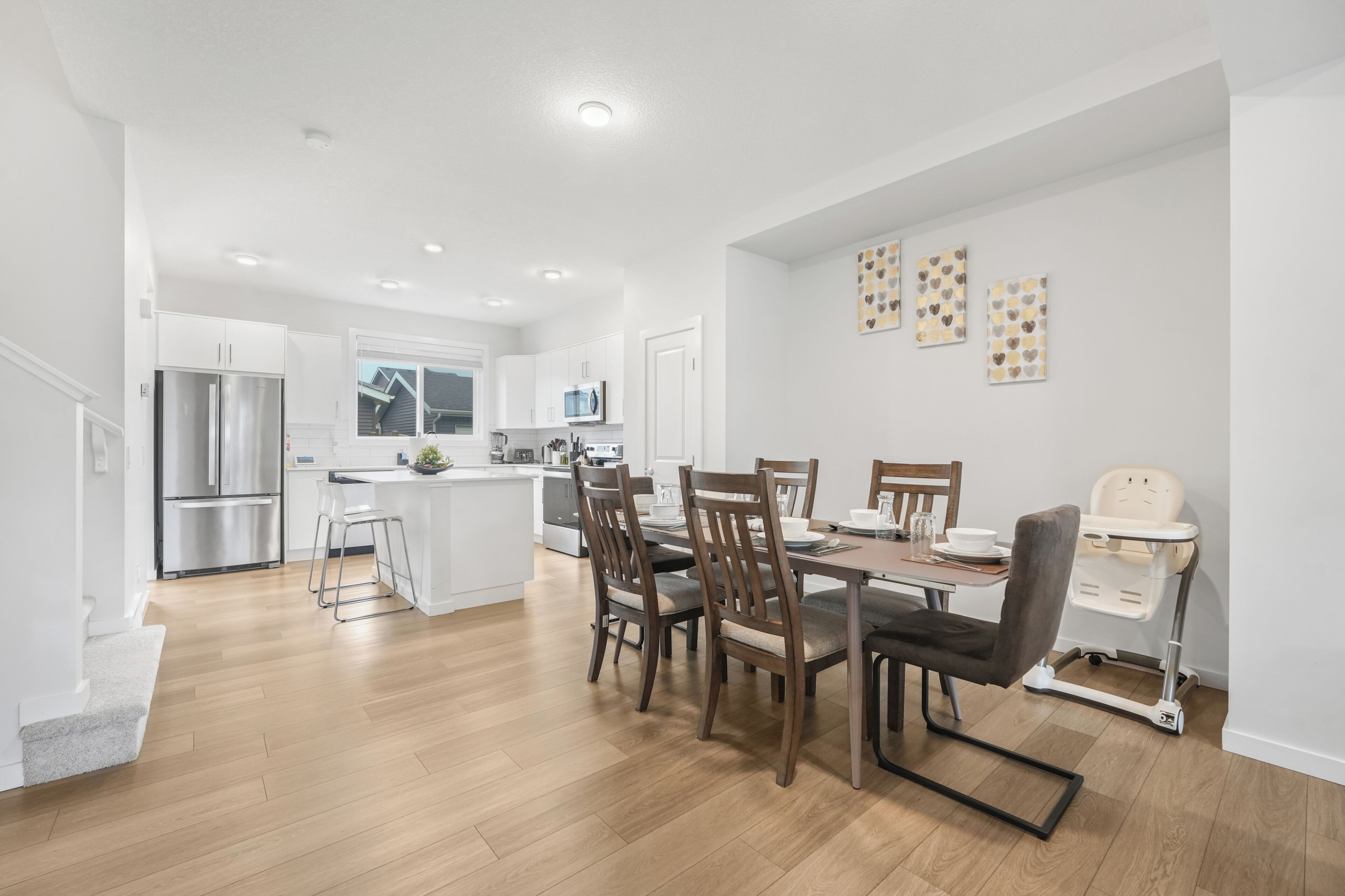 A modern kitchen with white cabinetry, a central island, and a dining area with wooden chairs and a high chair.