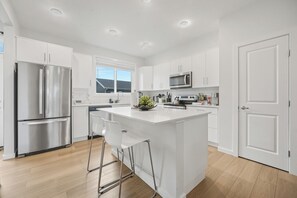 Une cuisine moderne avec des meubles blancs, des appareils en acier inoxydable et un îlot central doté de tabourets de bar.
