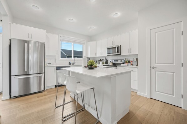 A modern kitchen with white cabinetry, stainless steel appliances, and a central island with bar stools.