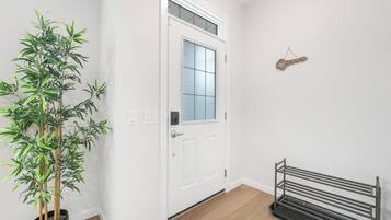 A clean hallway with a white door, a bamboo plant, a metal bench, and a wall-mounted key holder.