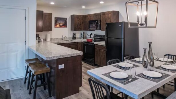 A modern kitchen with dark wood cabinets, a granite countertop, and a dining area set for four. - 4-B The Slick Rock Condo (Ground Floor/Pool Side) (Moab)