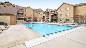A pool area with a clear blue pool, lounge chairs, and a stone wall backdrop. - 4-B The Slick Rock Condo (Ground Floor/Pool Side) (Moab)