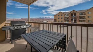 A balcony with a grill and table, overlooking a mountainous landscape and a building with multiple floors. - 4-E The Hidden Valley Condo (Second Floor/Parking Lot Side) (Moab)