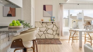 Una cocina moderna con protector contra salpicaduras de piedra, un comedor con mesa y sillas blancas, y vistas al exterior.