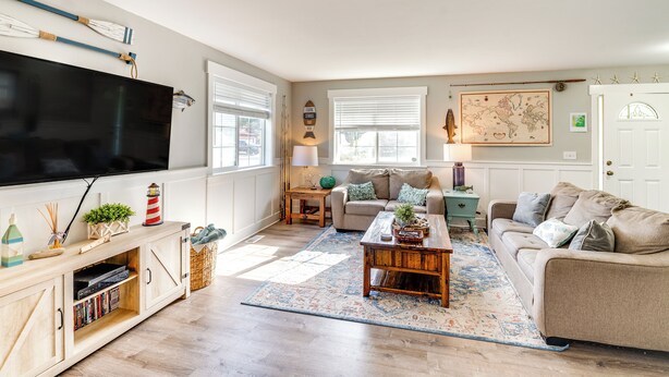 Een woonkamer met een flatscreen televisie, een houten entertainmentkast, een beige bank, een salontafel en een kamerkleed met een patroon.