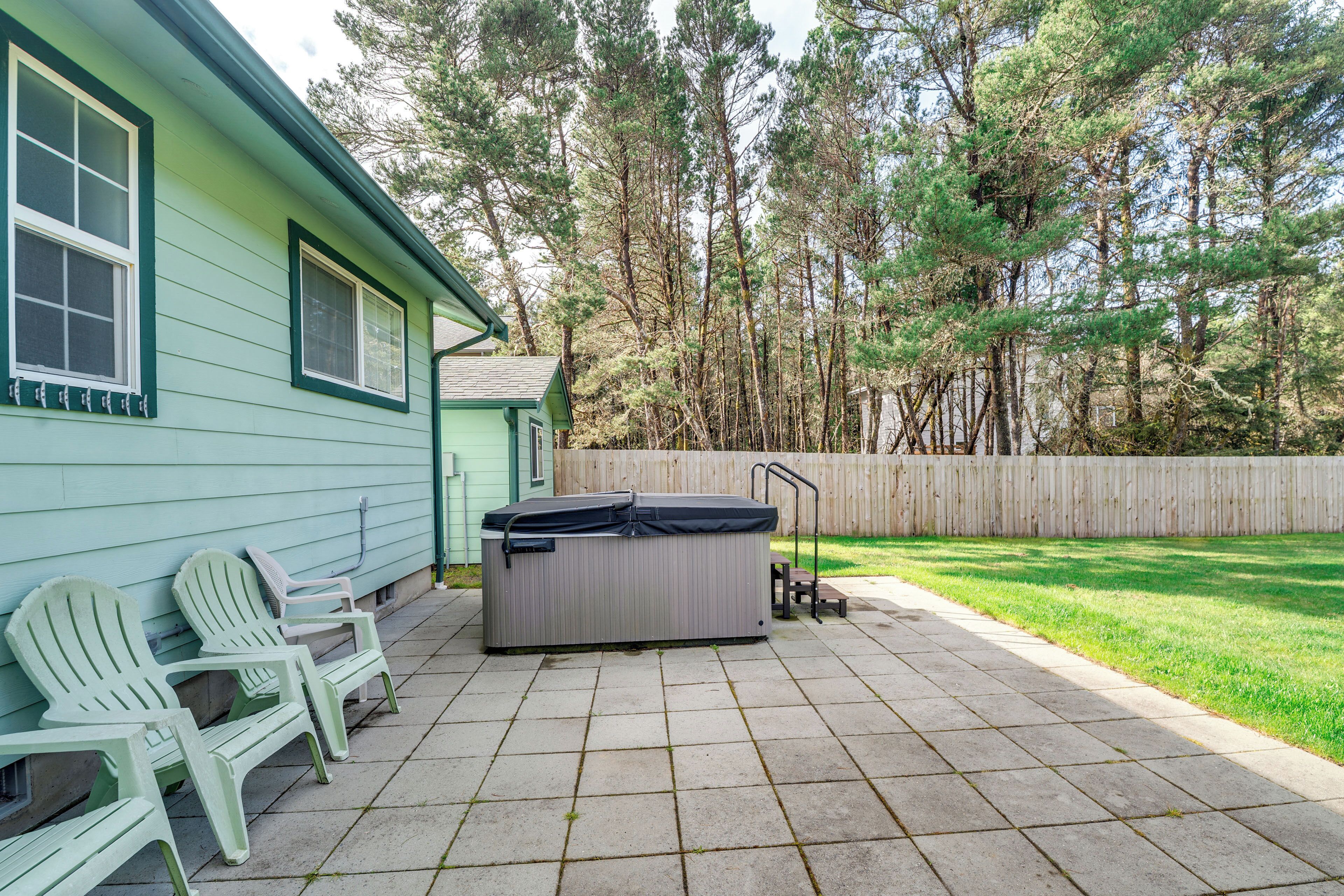 A patio with a hot tub, Adirondack chairs, and a wooden fence.