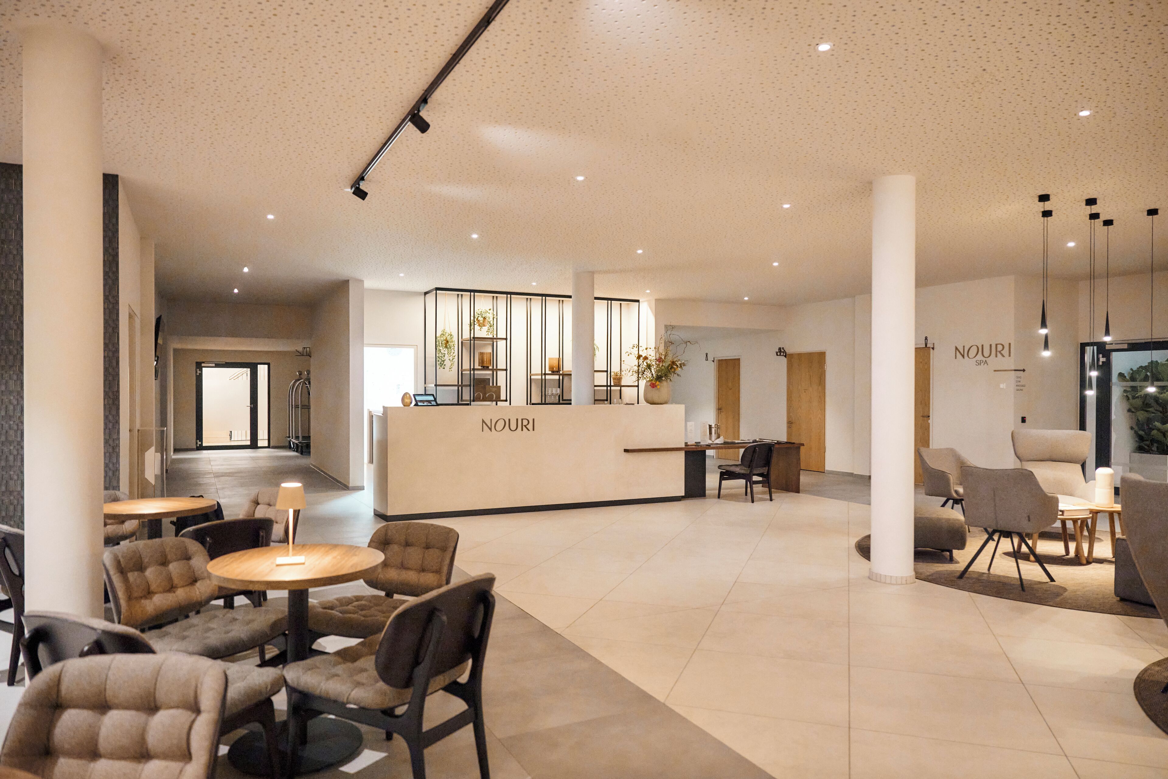 A spacious lobby with a reception desk labeled "NOURI," several seating areas, and a modern ceiling design.