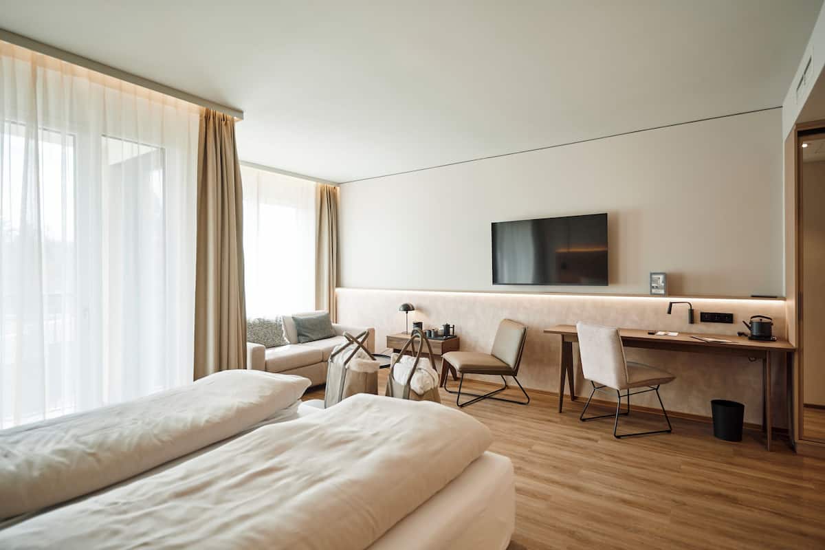 A modern hotel room with a large bed, a desk, a chair, and a TV mounted on the wall.