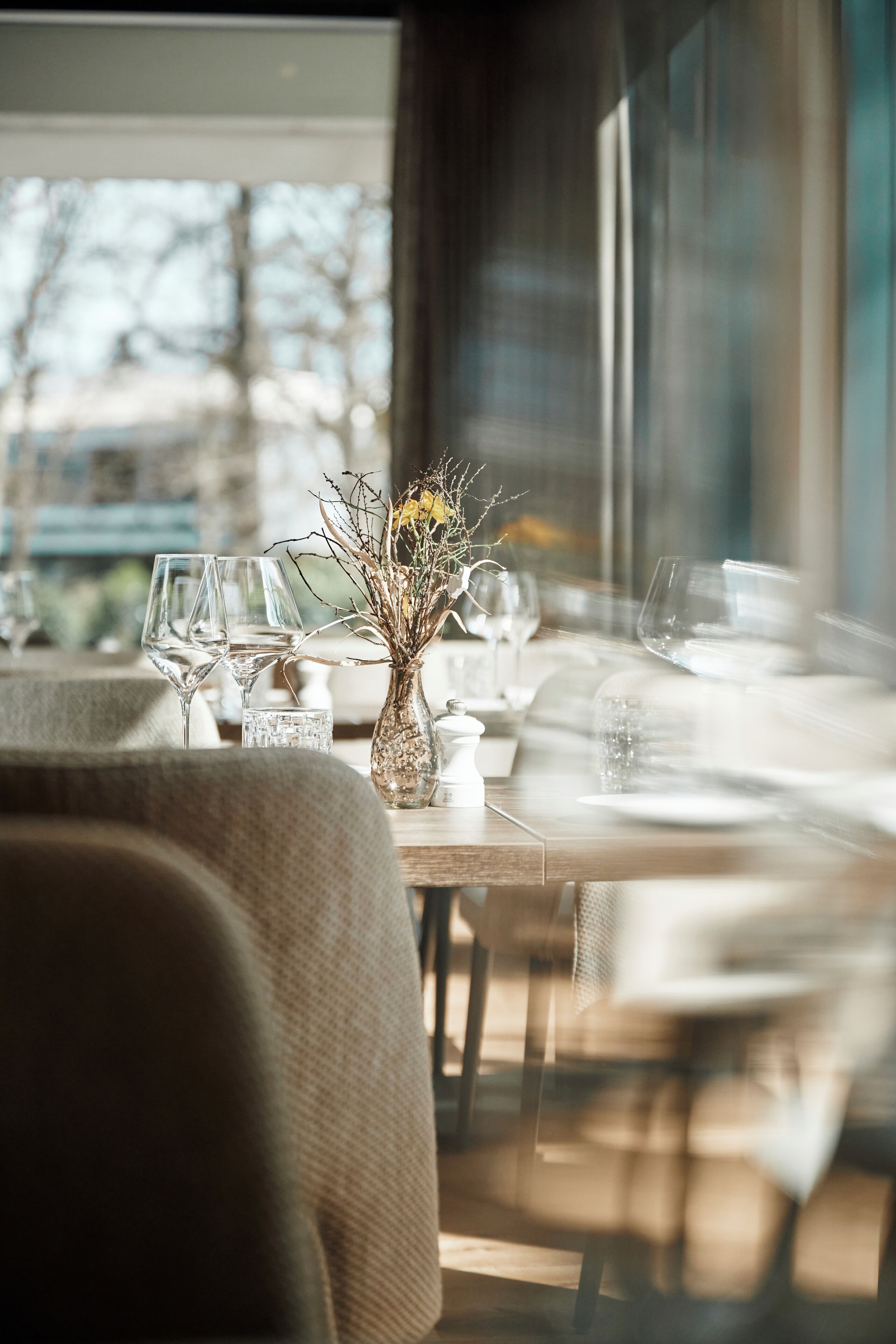 A dining table set with glasses and a vase of dried branches.