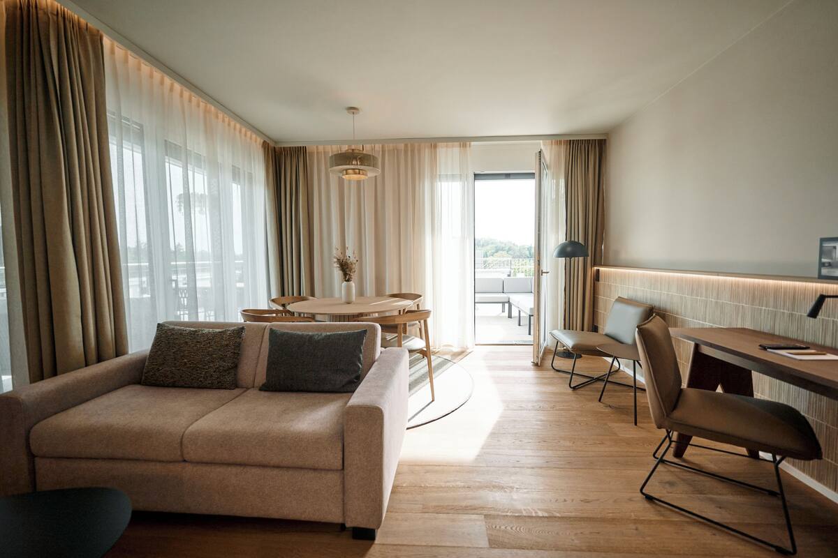 A modern hotel room with a sofa, dining table, and chairs.