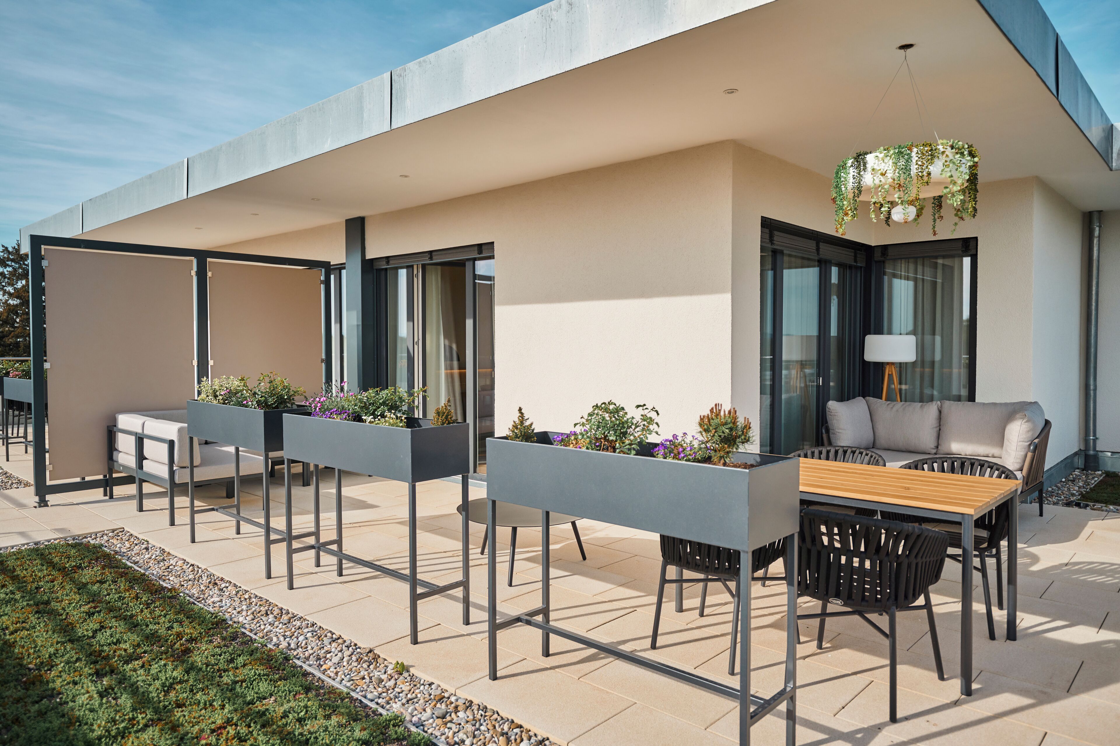 Une terrasse extérieure avec une table et des chaises en bois, des jardinières fleuries et un luminaire suspendu.