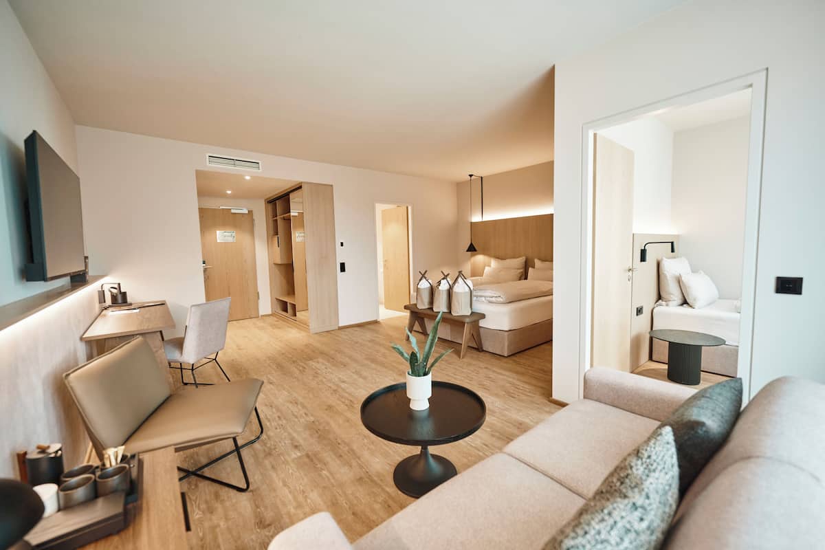 A modern living room with a sofa, a coffee table, and a TV mounted on the wall. There is a wooden floor and a door leading to another room.