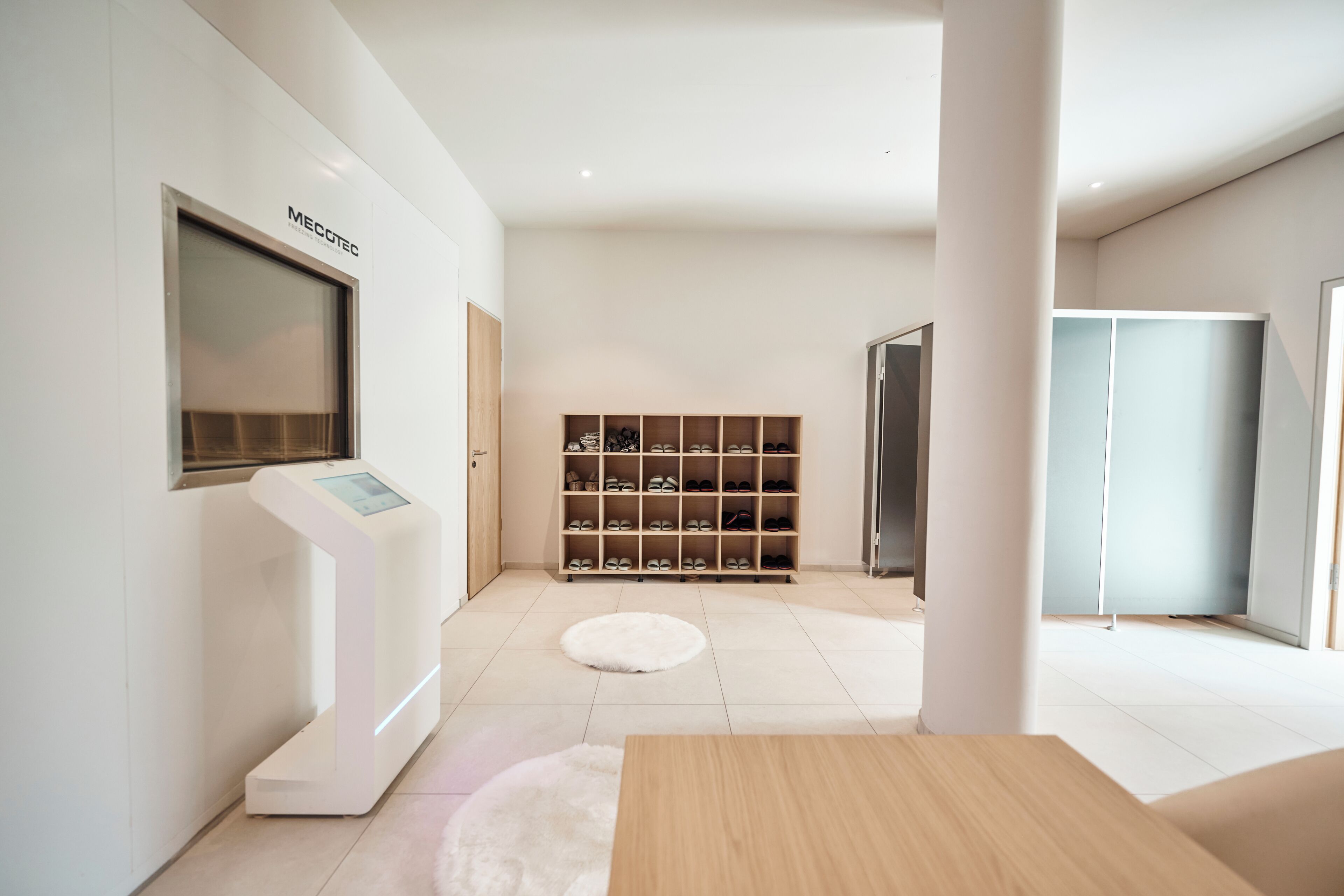 A modern, minimalist room with a shoe storage unit, a wooden table, and a white rug.