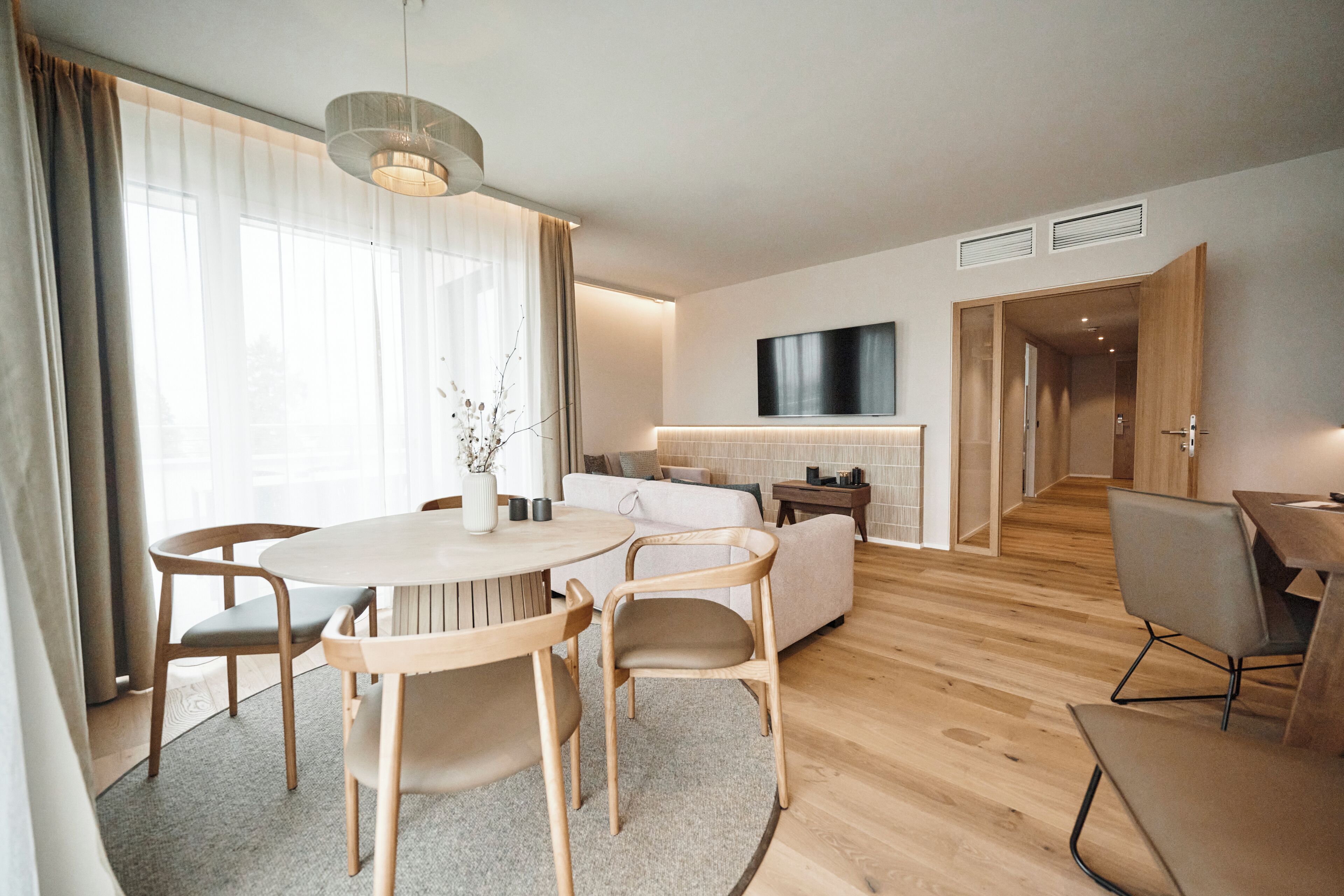 Un salon moderne avec une table de salle à manger ronde, deux chaises, un canapé et un téléviseur fixé au mur.